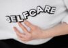 Close-up of a hand holding the word 'self-care' made with 3D letters on a white background.