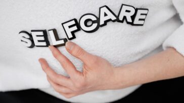 Close-up of a hand holding the word 'self-care' made with 3D letters on a white background.