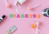 Flat lay image depicting diabetes with glucometer, pills, and lollipops on a pink background.