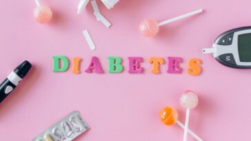 Flat lay image depicting diabetes with glucometer, pills, and lollipops on a pink background.